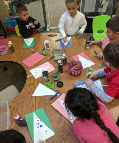 A group of children are sitting around a table with papers scissors and glue