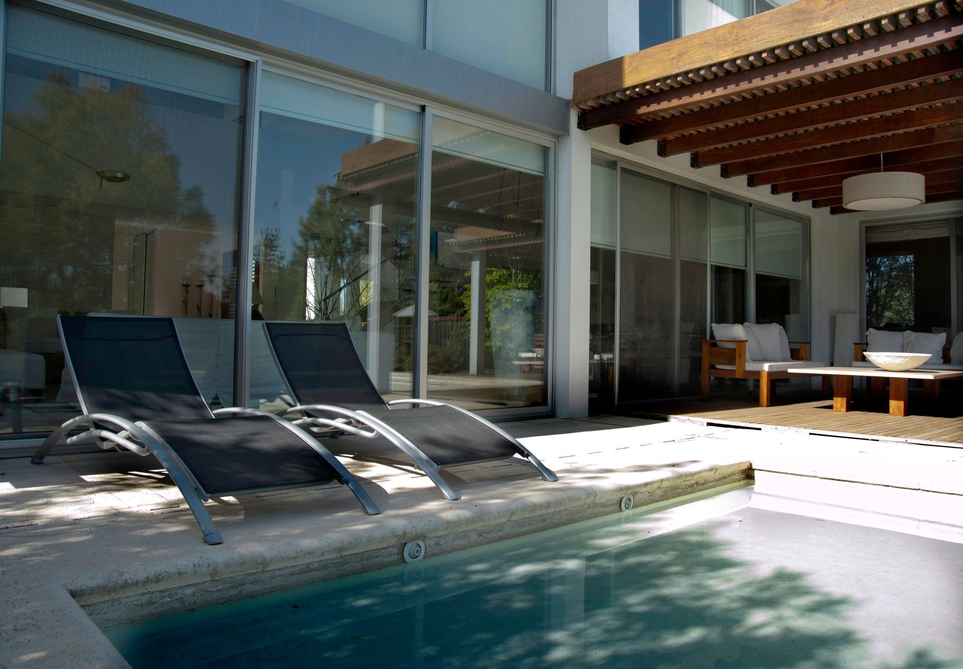 Tumbonas junto a la piscina y casa moderna con pérgola.