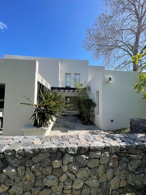 Casa moderna blanca con un muro de piedra en el frente; cielo azul brillante.