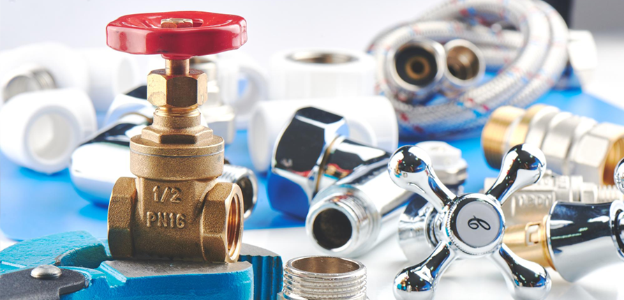 Various plumbing supplies, including a red-handled valve, chrome faucets, and piping components, arranged on a blue surface.
