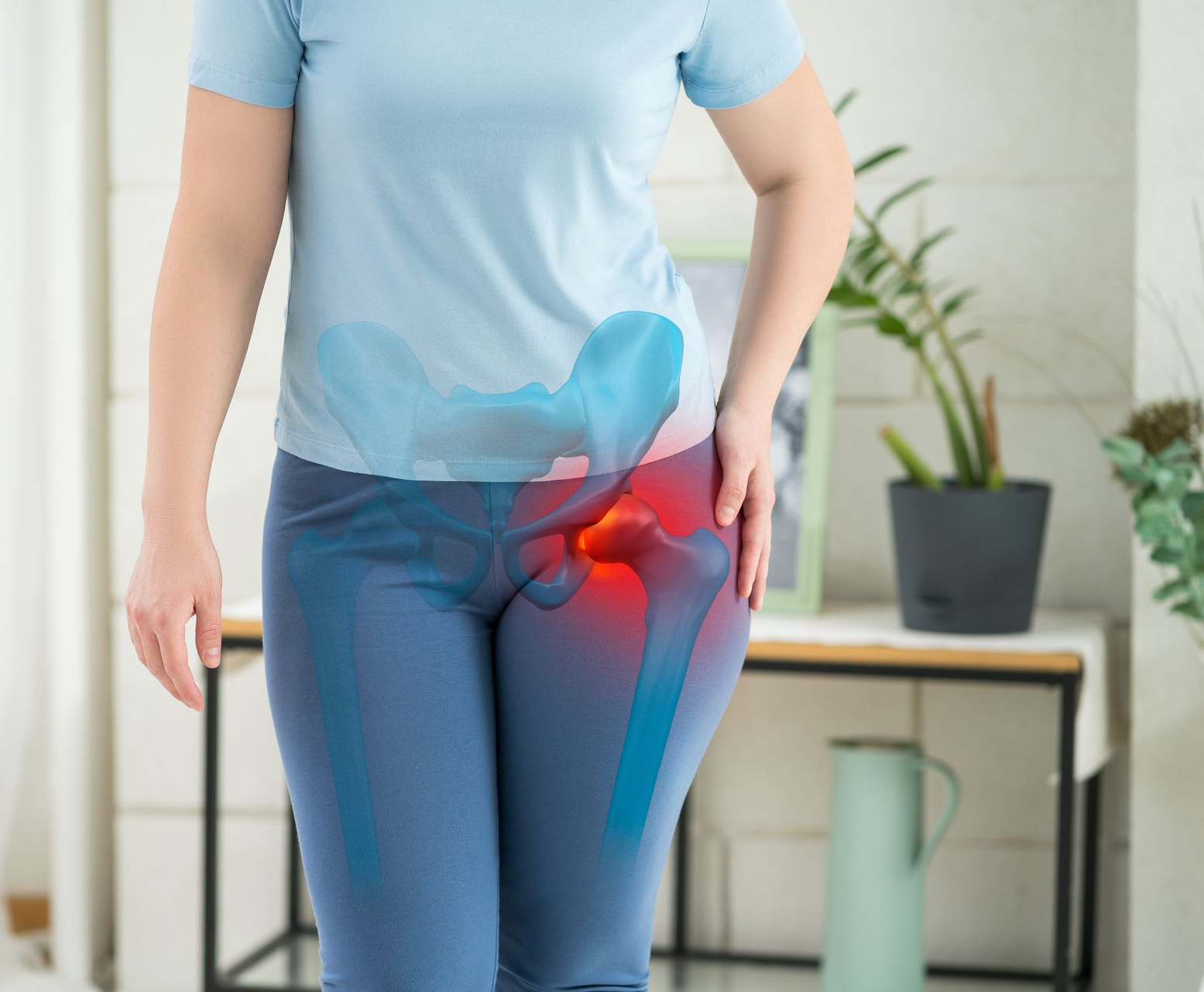 Person holding hip with highlighted pain area, standing indoors near a table and plant.