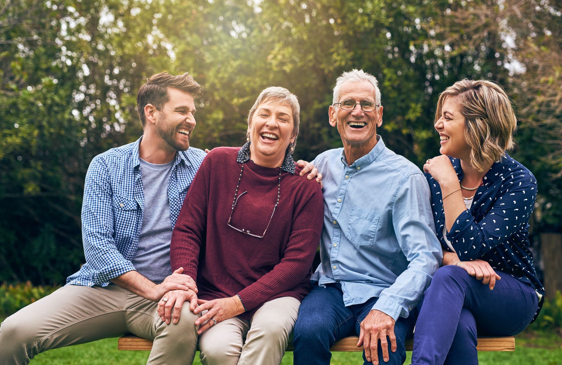 Four people sitting on a park bench, smiling and laughing together outdoors