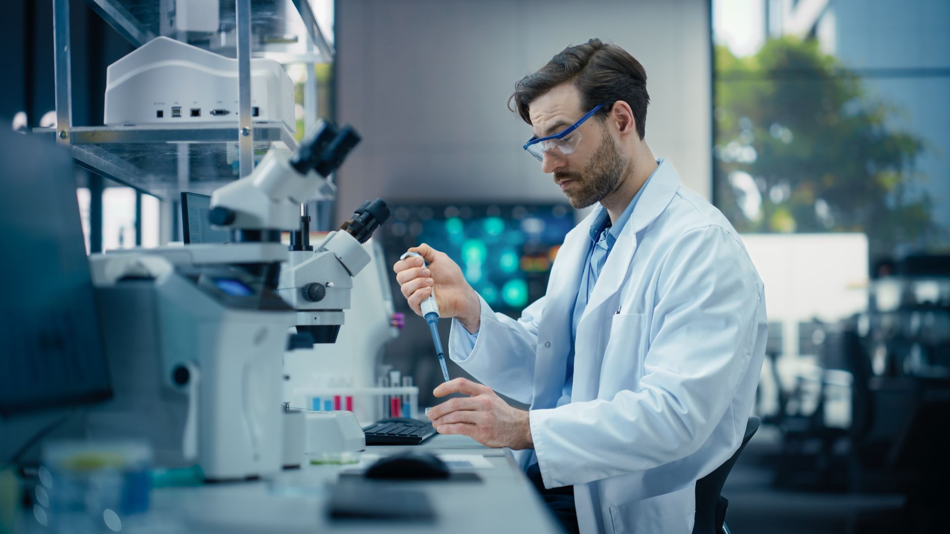 Scientist in a lab coat using a pipette at a laboratory bench with microscopy equipment