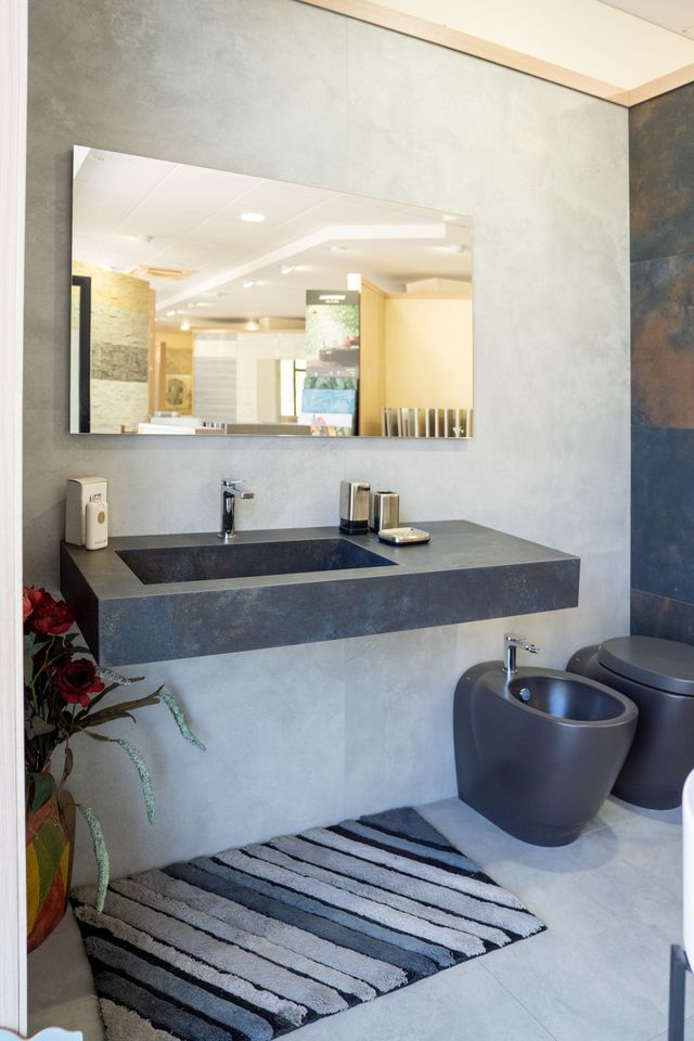 Modern bathroom with dark walls, wooden counter, round mirror, and a small chair.