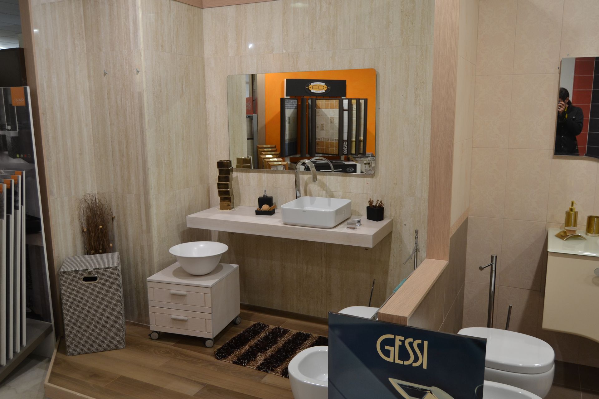Bathroom display with white sink, mirror, and toilet. Beige walls and cabinet.