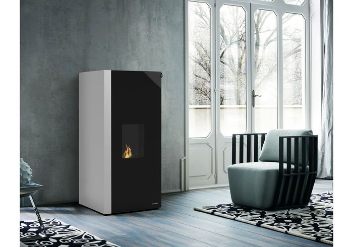 Modern white and black pellet stove in a living room, near a window and an armchair.