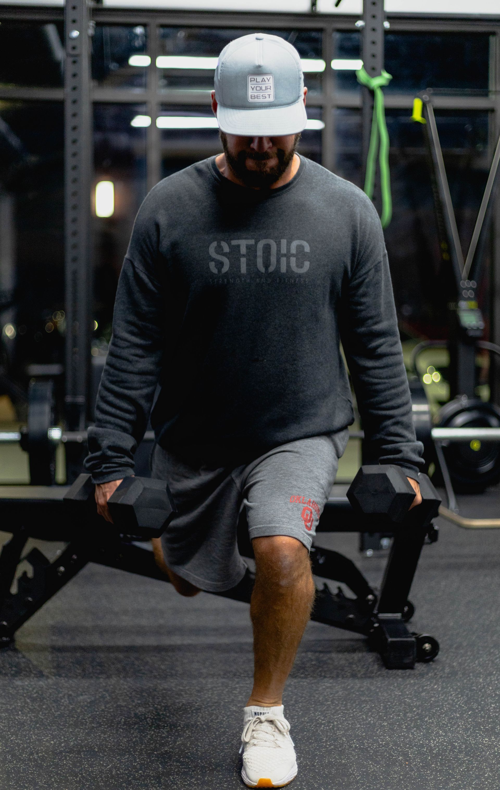 A man is sitting on a bench in a gym holding a dumbbell.