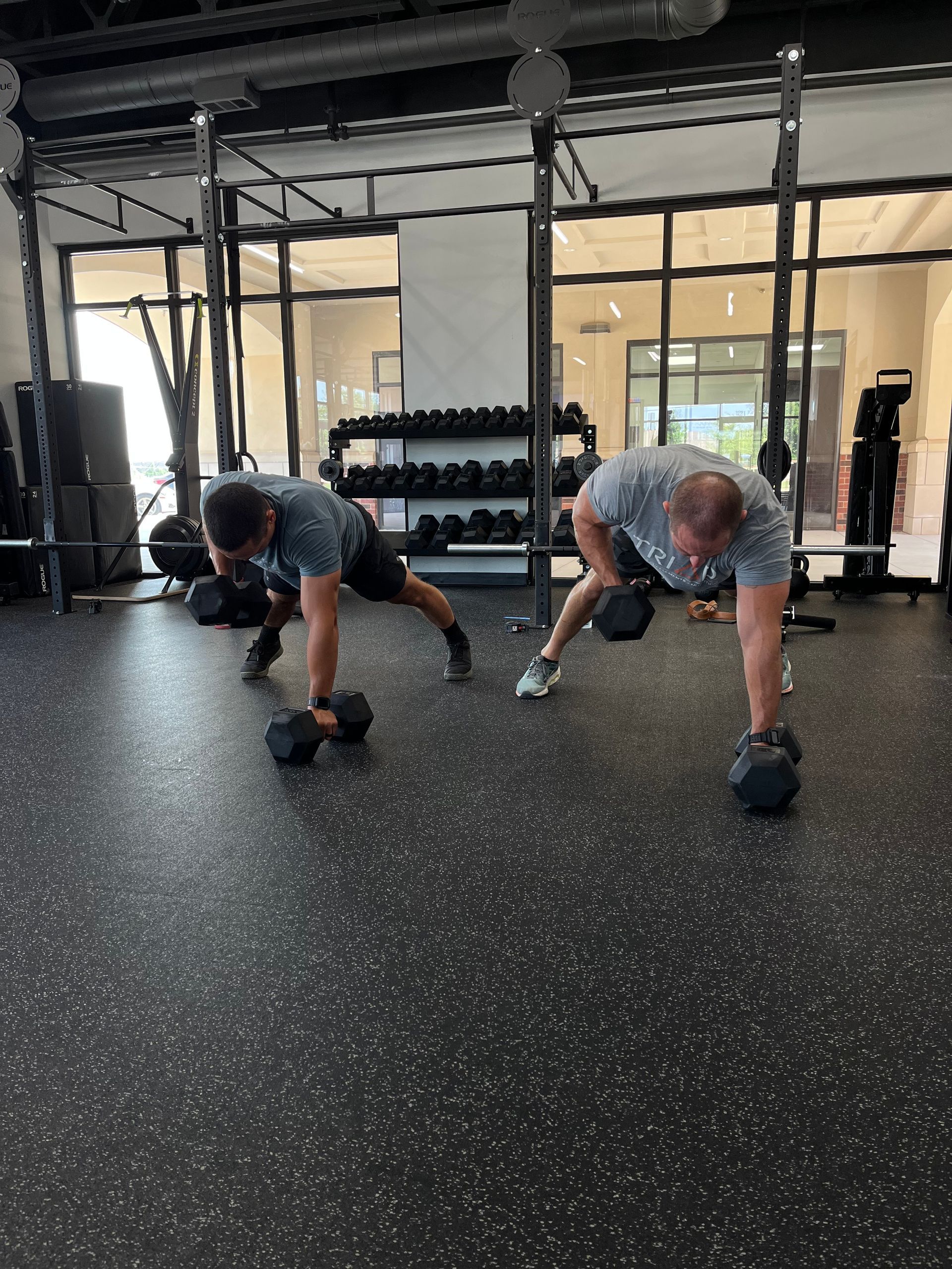 Two men are doing push ups with dumbbells in a gym.