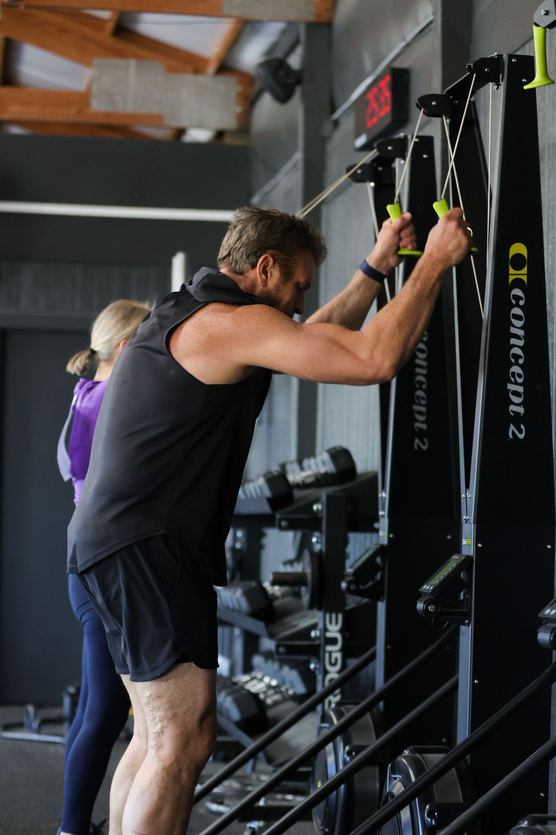 A man is sitting on a bench in a gym holding a dumbbell.