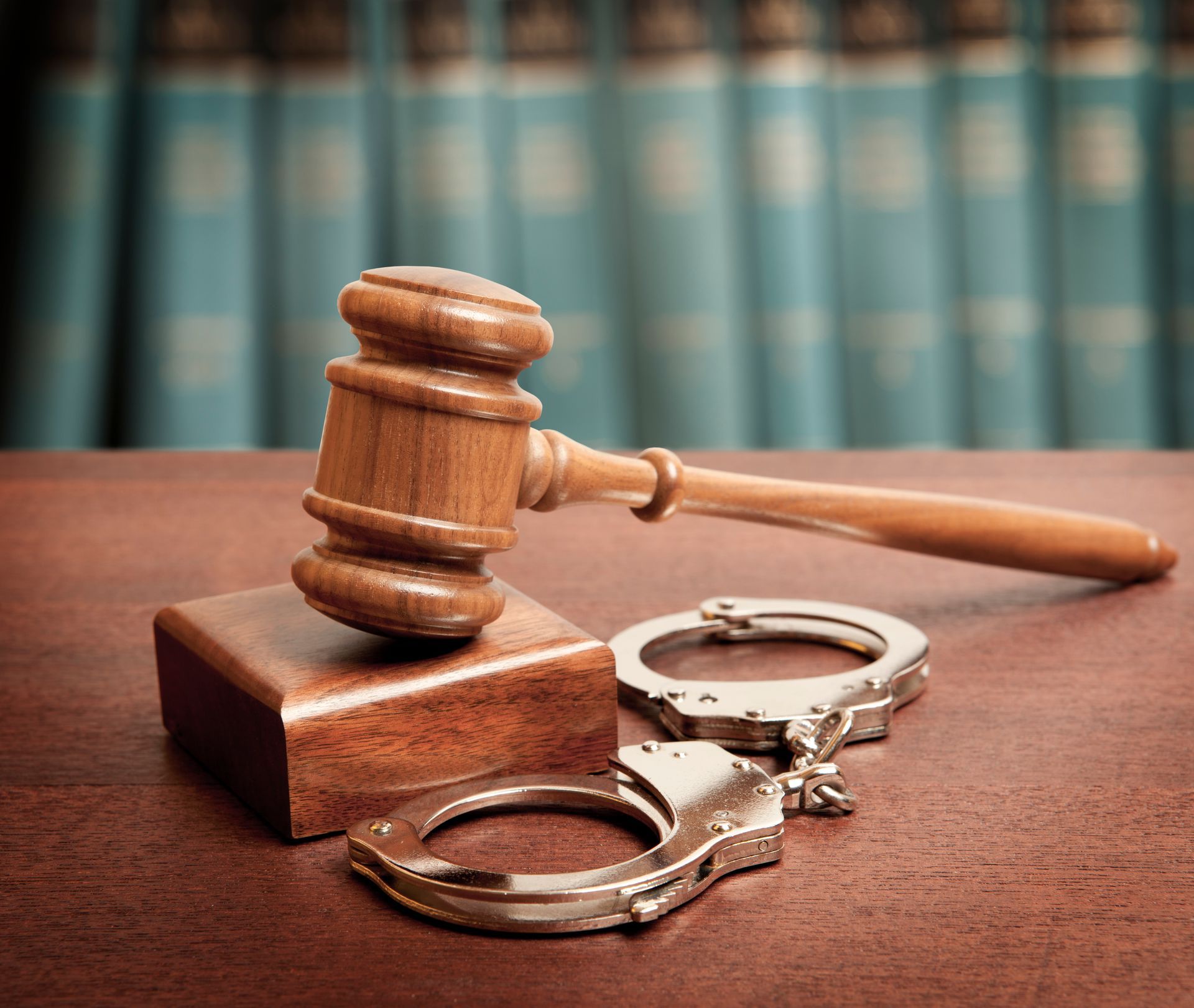 A wooden judge 's gavel and handcuffs are on a wooden table.