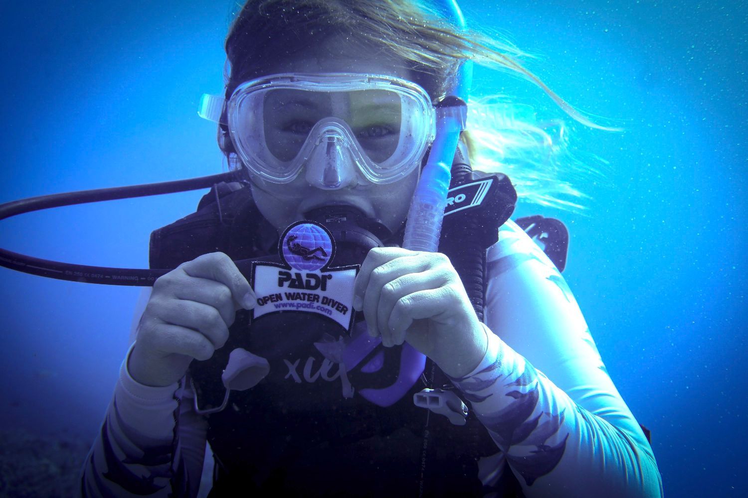 A woman wearing a scuba diving mask and goggles is holding a card that says padi