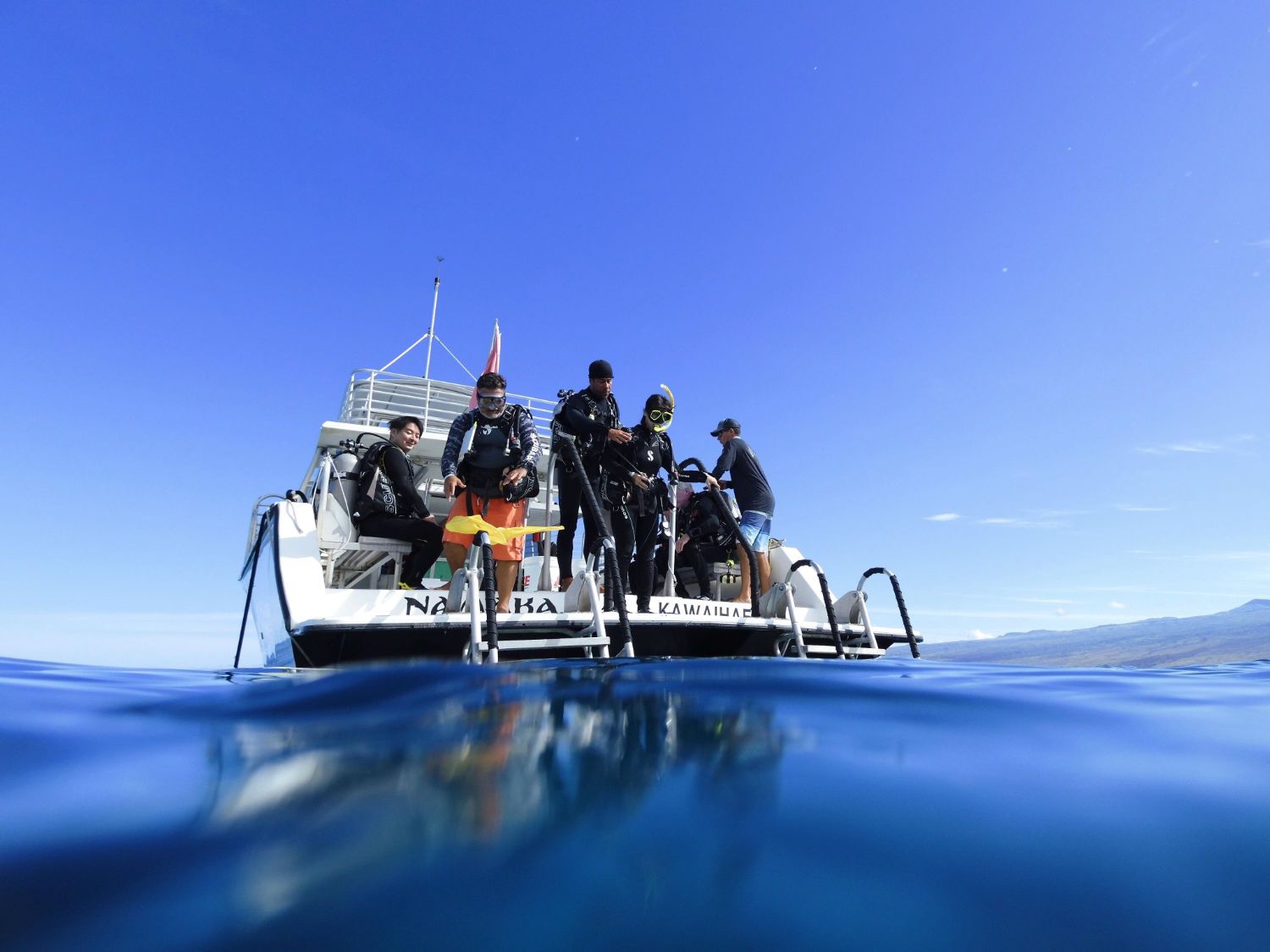 A group of people are standing on the back of a boat in the ocean.