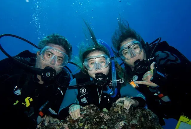 Three scuba divers are posing for a picture in the ocean.
