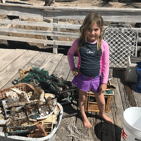 A little girl is standing on a wooden deck next to a pile of trash.