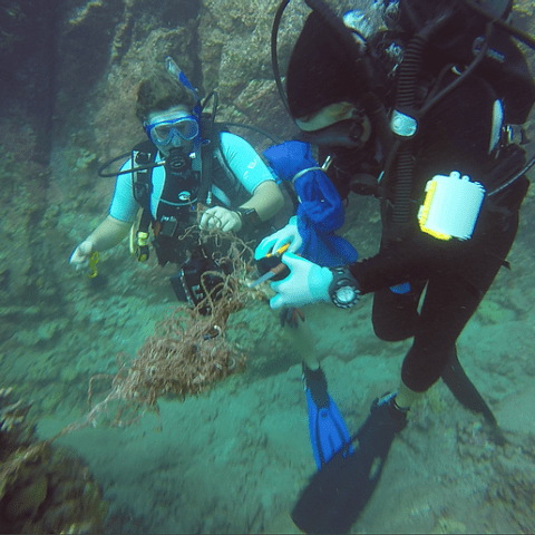 Two scuba divers are holding a piece of trash in their hands