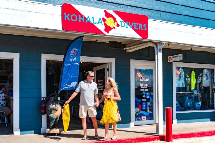 A man and a woman are walking in front of the dive shop. 