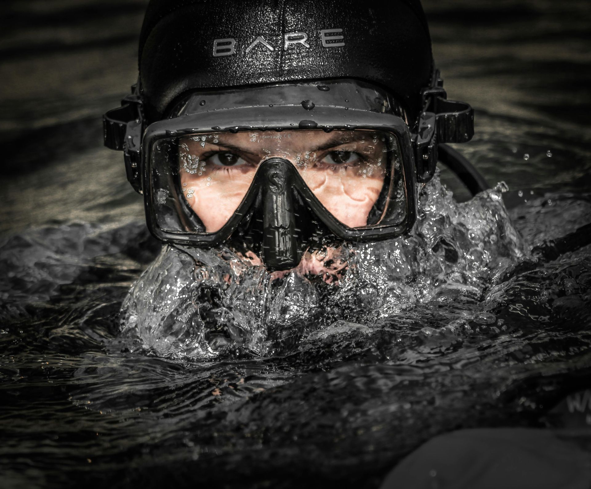 A person wearing a bare helmet and mask is swimming in the water