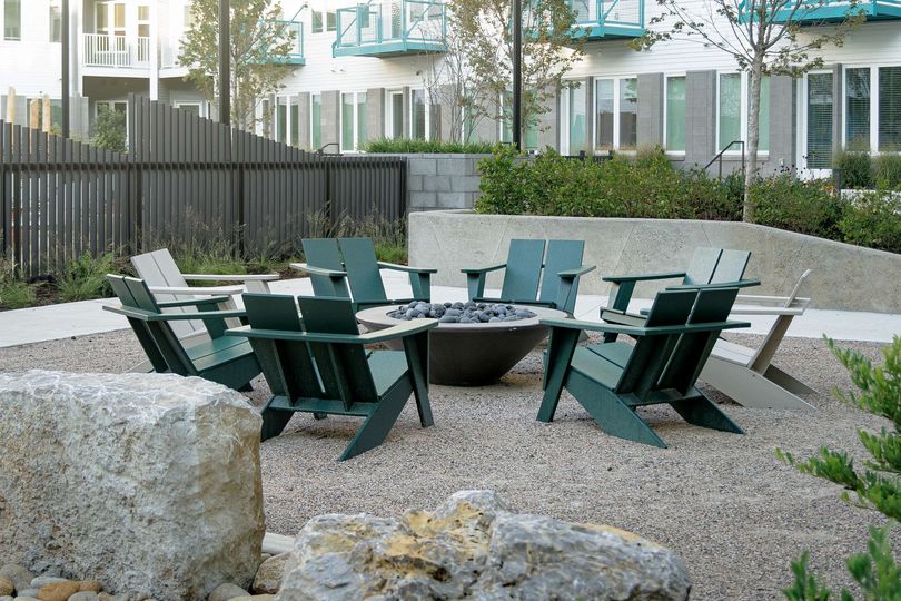 Circular green chairs around a fire pit in a gravel courtyard with apartment buildings and rocks nearby