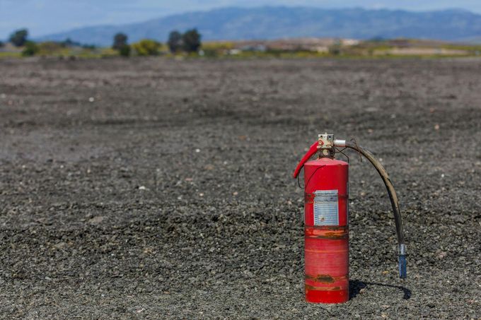 Red fire extinguisher on a gravel surface with a distant mountain range in the background.