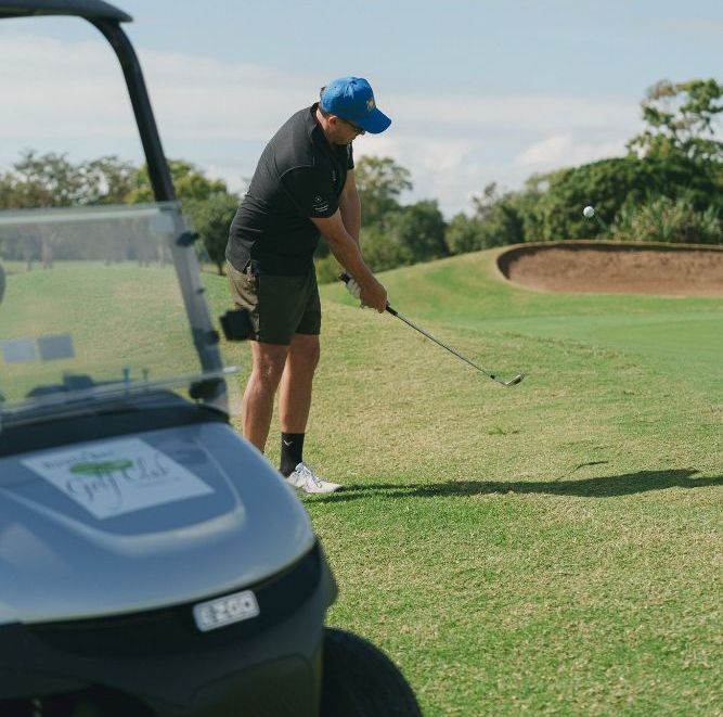 A man is swinging a golf club on a golf course next to a golf cart.— Rowes Bay Golf Club In Rowes Bay, QLD