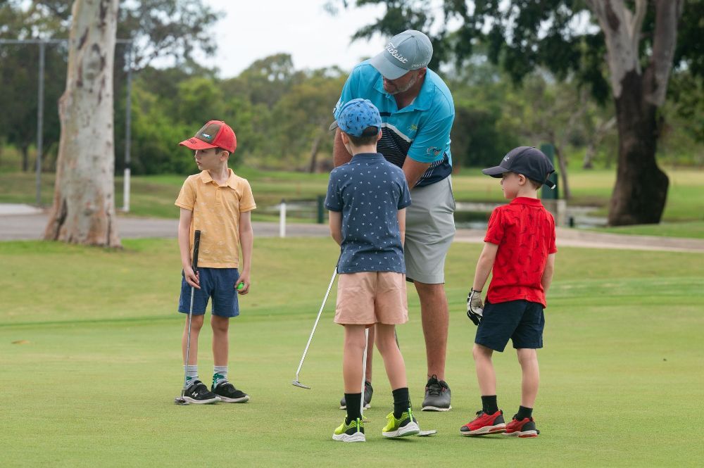 A man is teaching three young boys how to play golf on a golf course - — Rowes Bay Golf Club In Rowes Bay, QLD