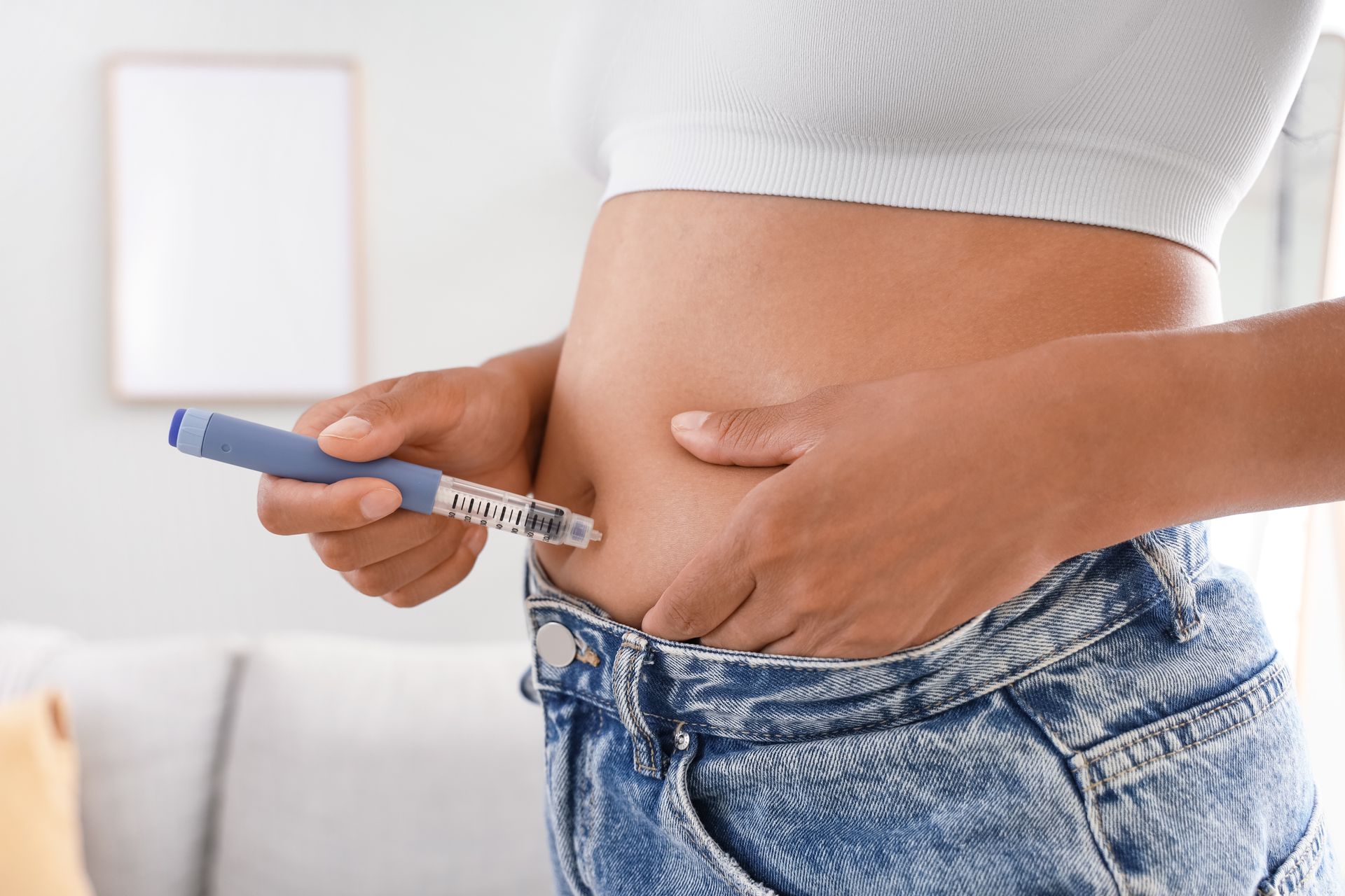 Person injecting insulin into abdomen with a syringe, wearing jeans and a white top
