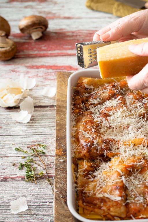 A person is grating cheese on top of a casserole dish.
