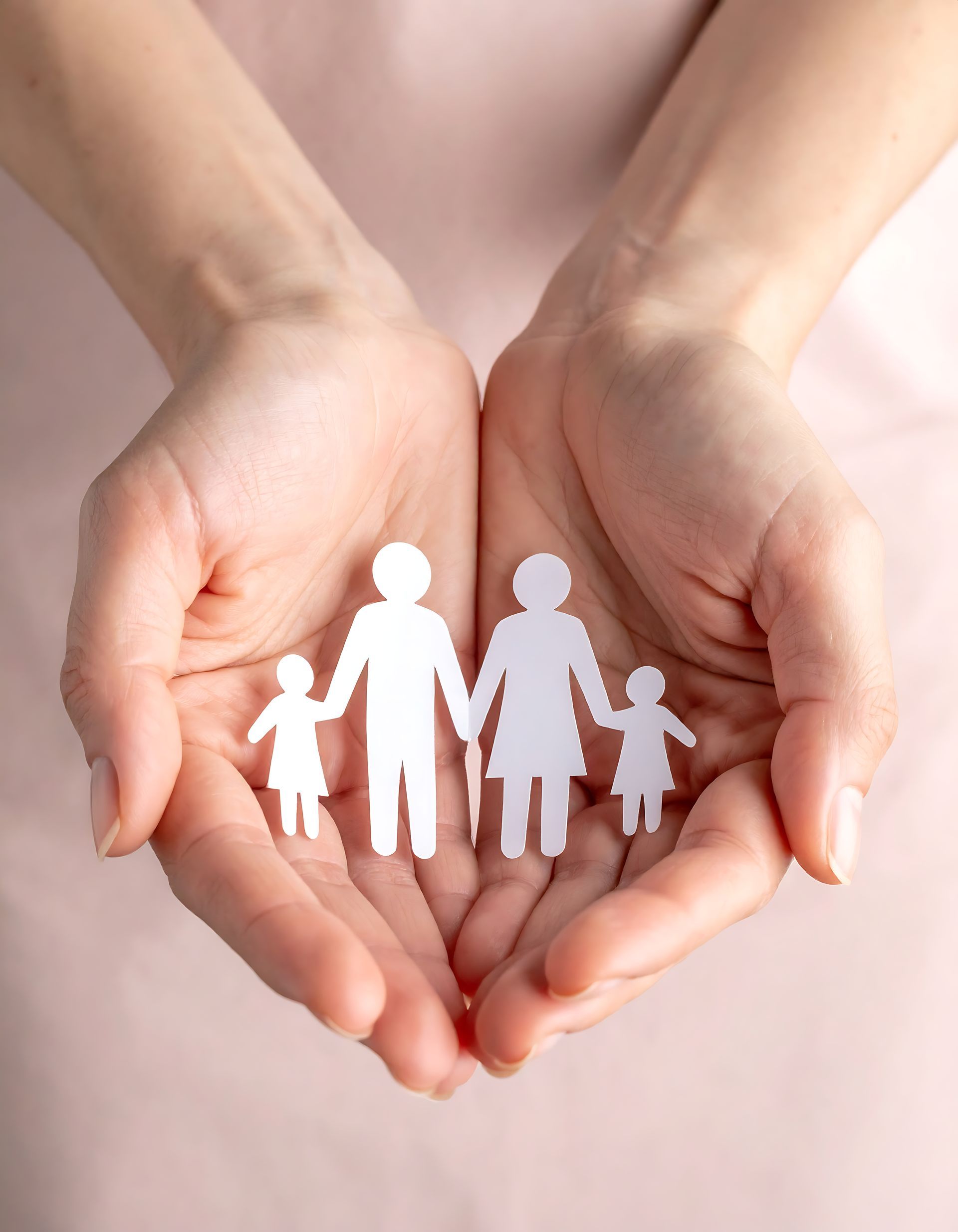 A pair of cupped hands holding a white paper cutout of a family of four.