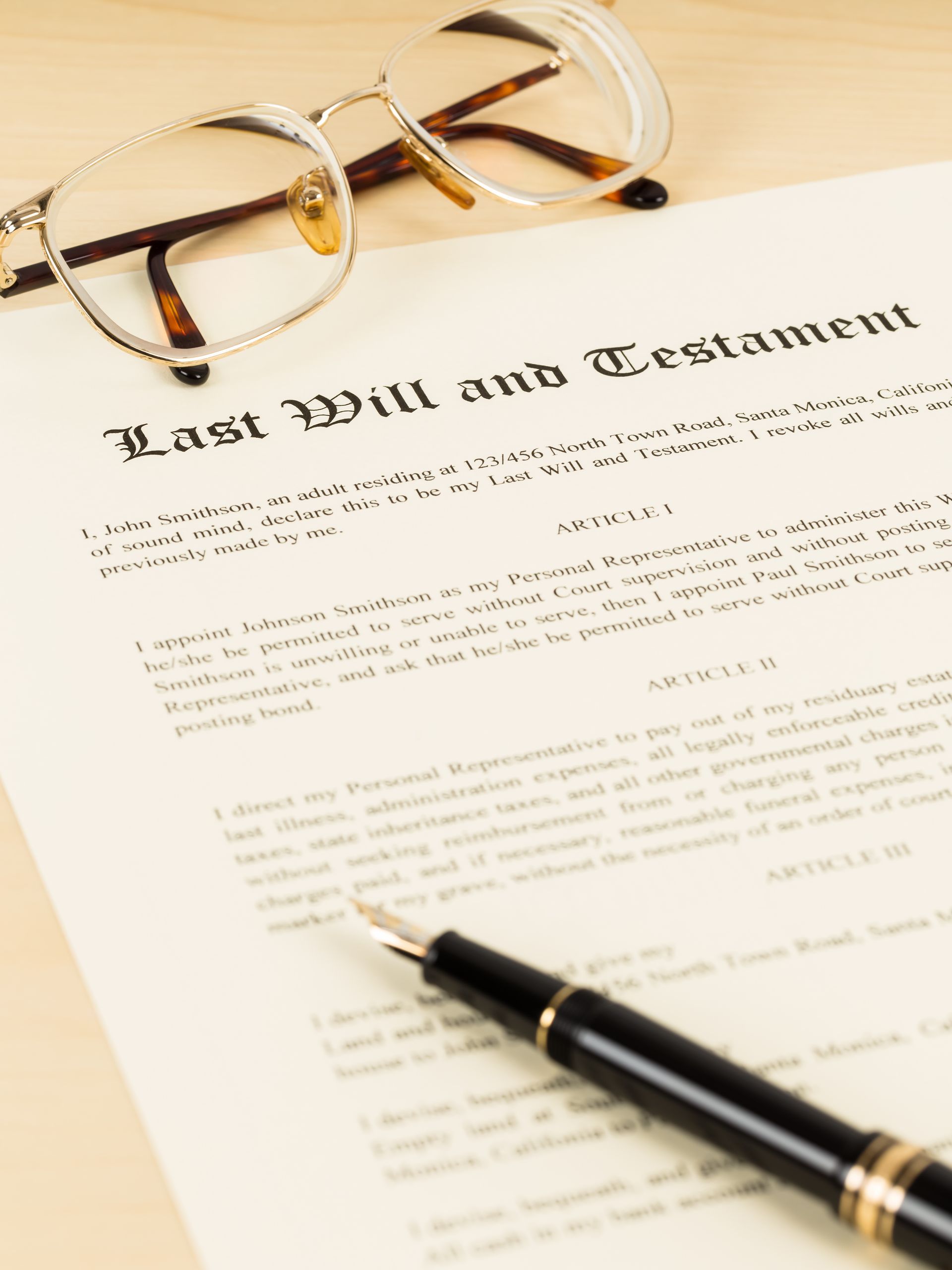 A pair of eyeglasses and a black fountain pen resting on a document titled Last Will and Testament. A pair of eyeglasses and a black fountain pen resting on a document titled Last Will and Testament.