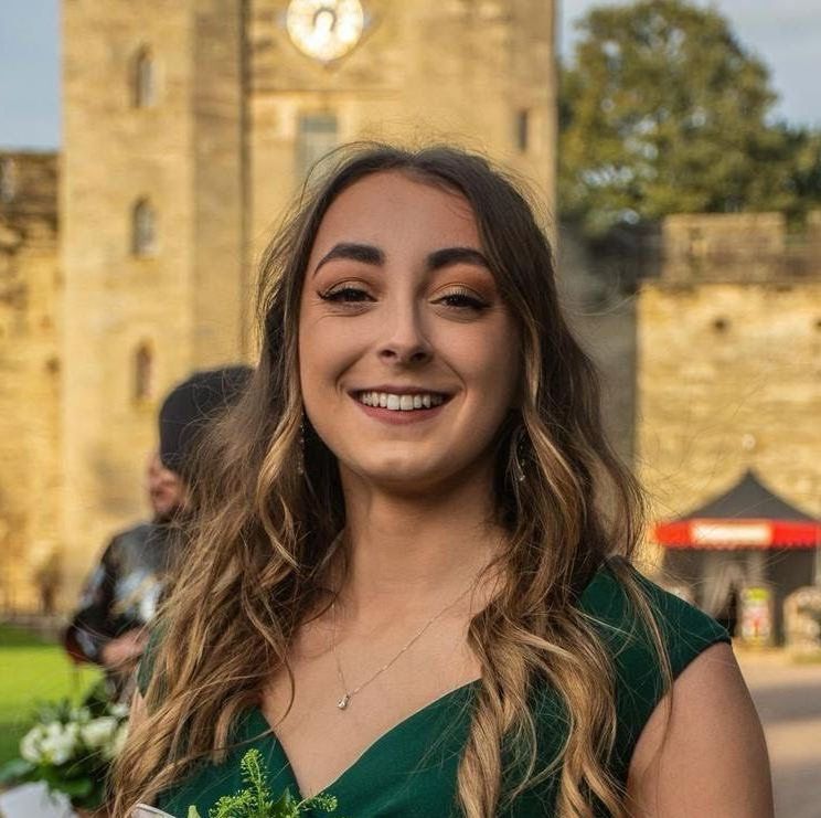 A woman in a green dress is smiling in front of a clock tower.