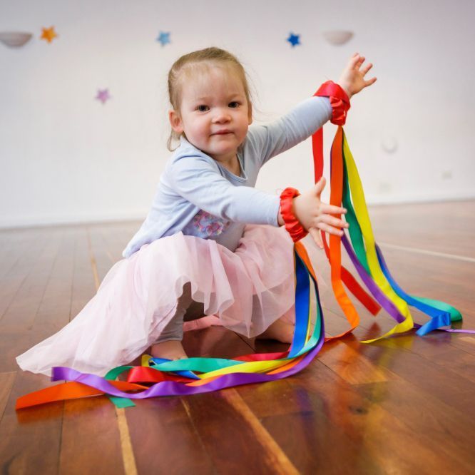 A little girl is sitting on the floor playing with ribbons