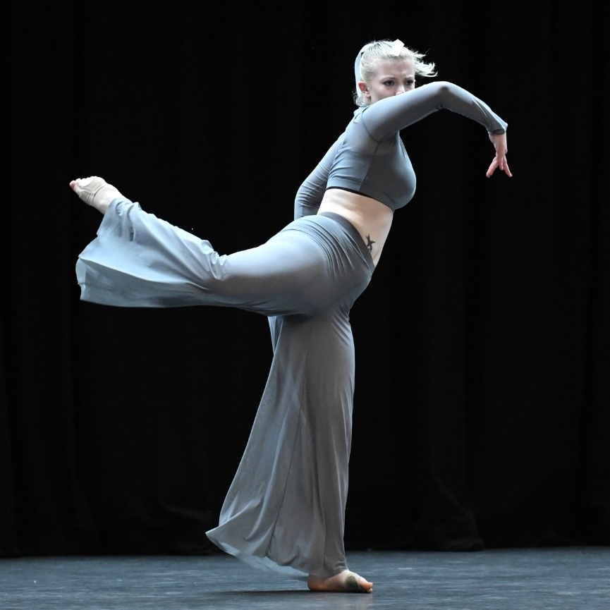 A woman in a black top and white pants is dancing on a stage