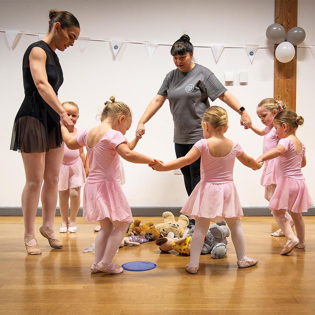 A group of young girls in pink tutus are holding hands in a circle.