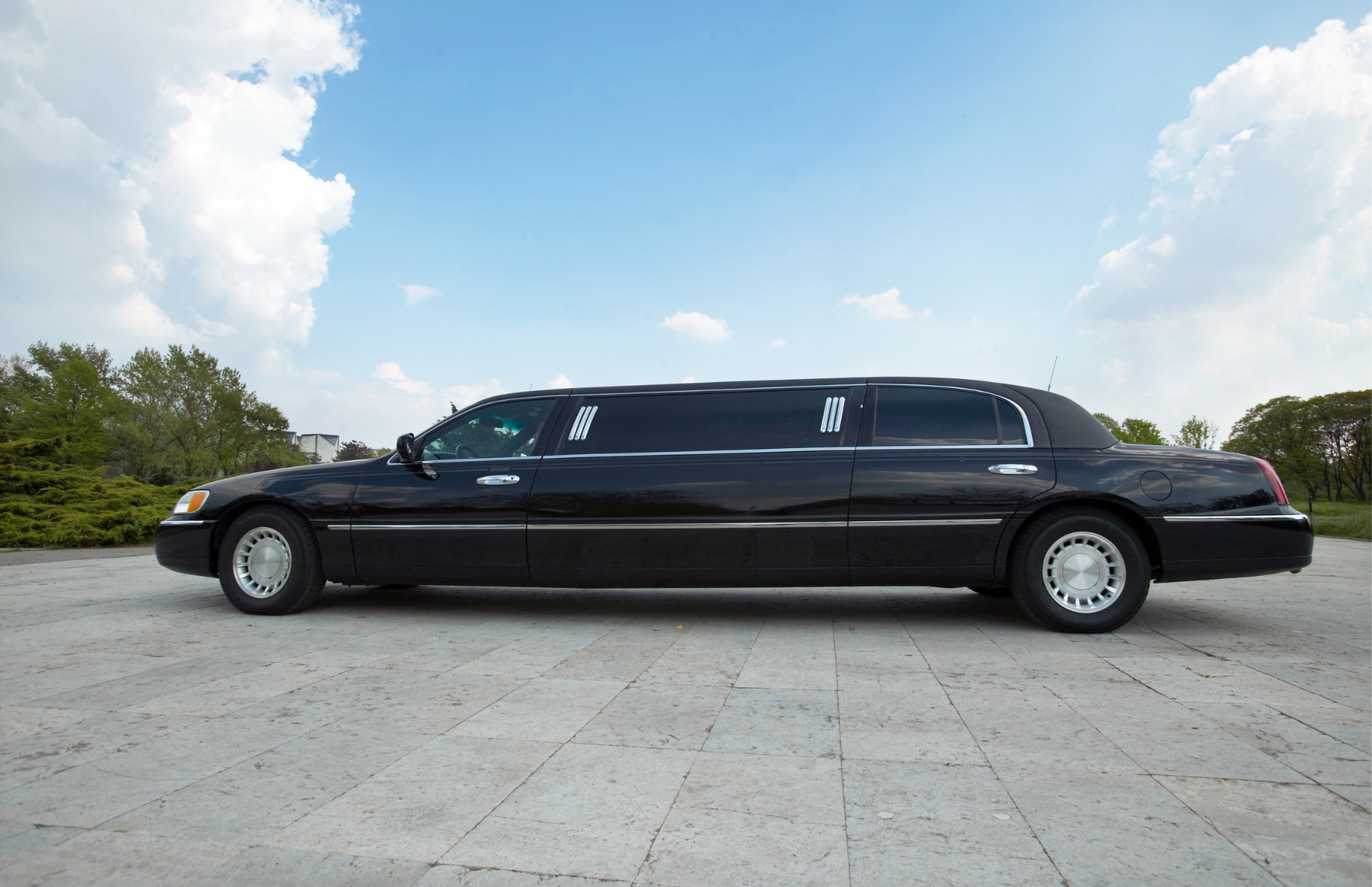 Black stretch limousine parked on a paved lot under a partly cloudy sky.