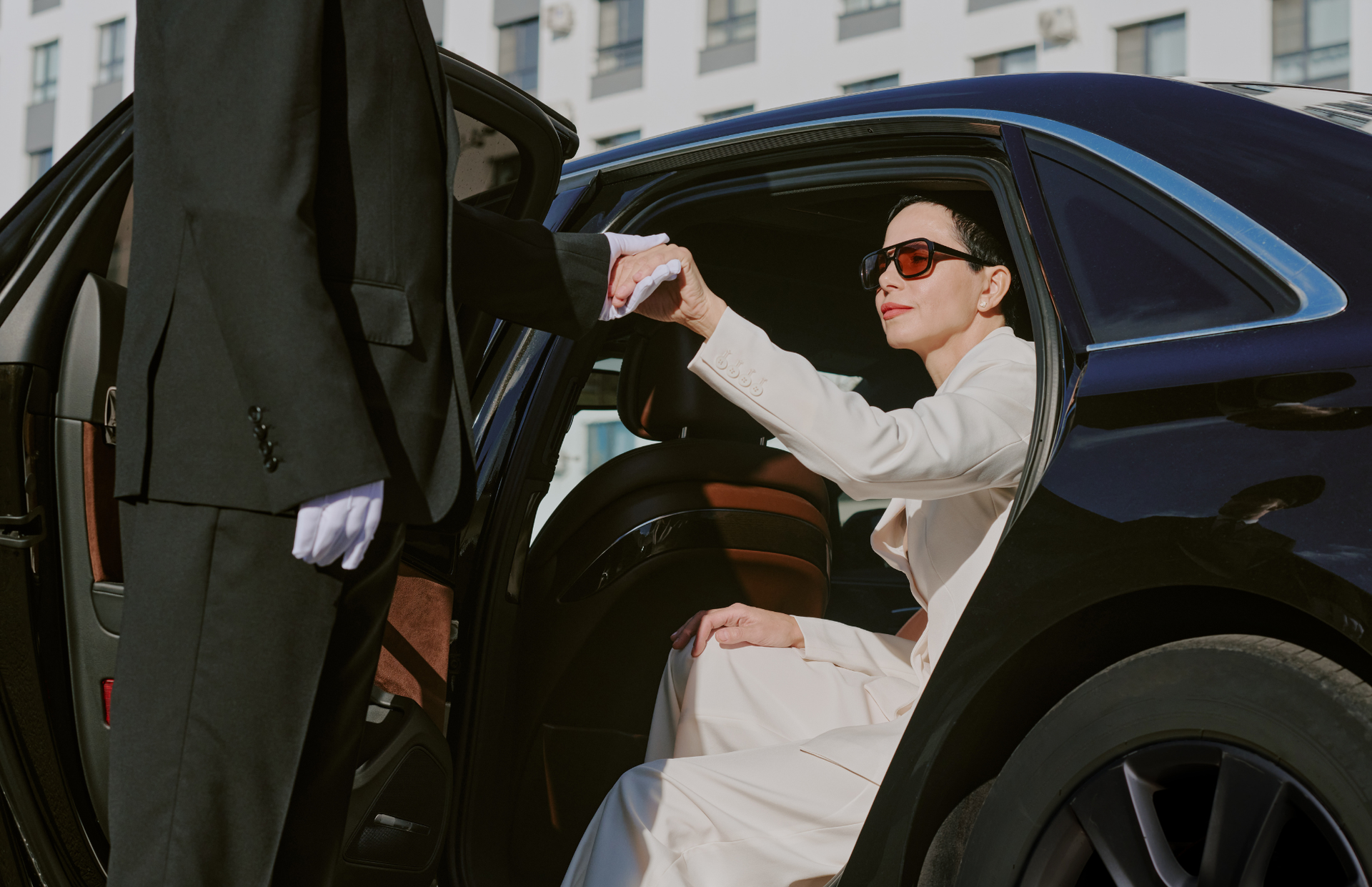 Woman in sunglasses gets into a black car while reaching for a hand from someone in black robes