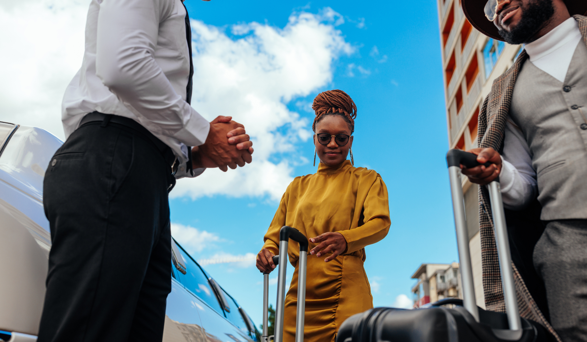Two people in business attire stand with a woman holding a suitcase in a city setting under a blue sky.