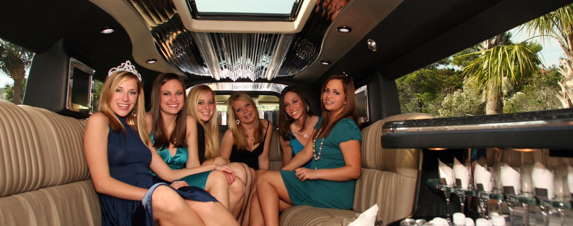 Five women sit smiling in a luxury limousine with champagne glasses and a sunroof view