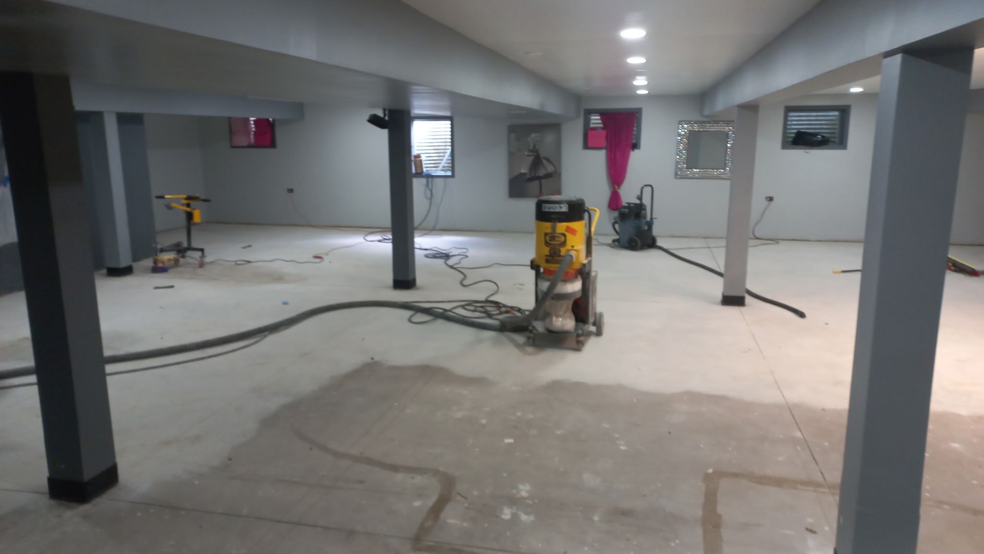 Basement construction area with concrete floor, support columns, and a floor grinder in the center.
