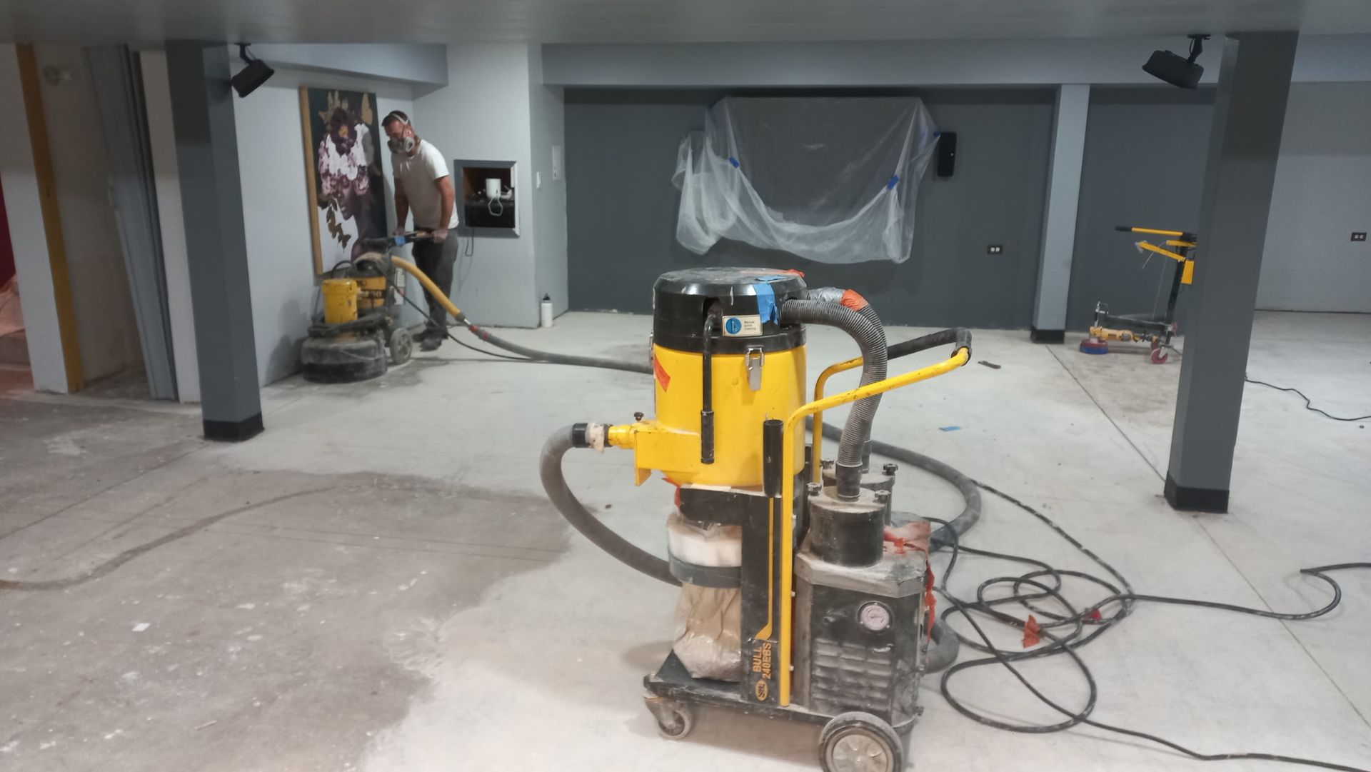 Basement garage with a yellow floor polisher, cords, and covered items in the background