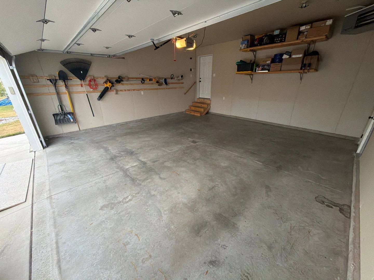 Empty garage interior with concrete floor, wall-mounted shelves, and overhead lights
