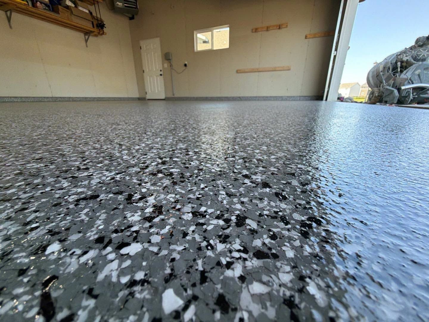Garage with freshly coated speckled epoxy floor, viewed low to the ground, with open door and tools at the side