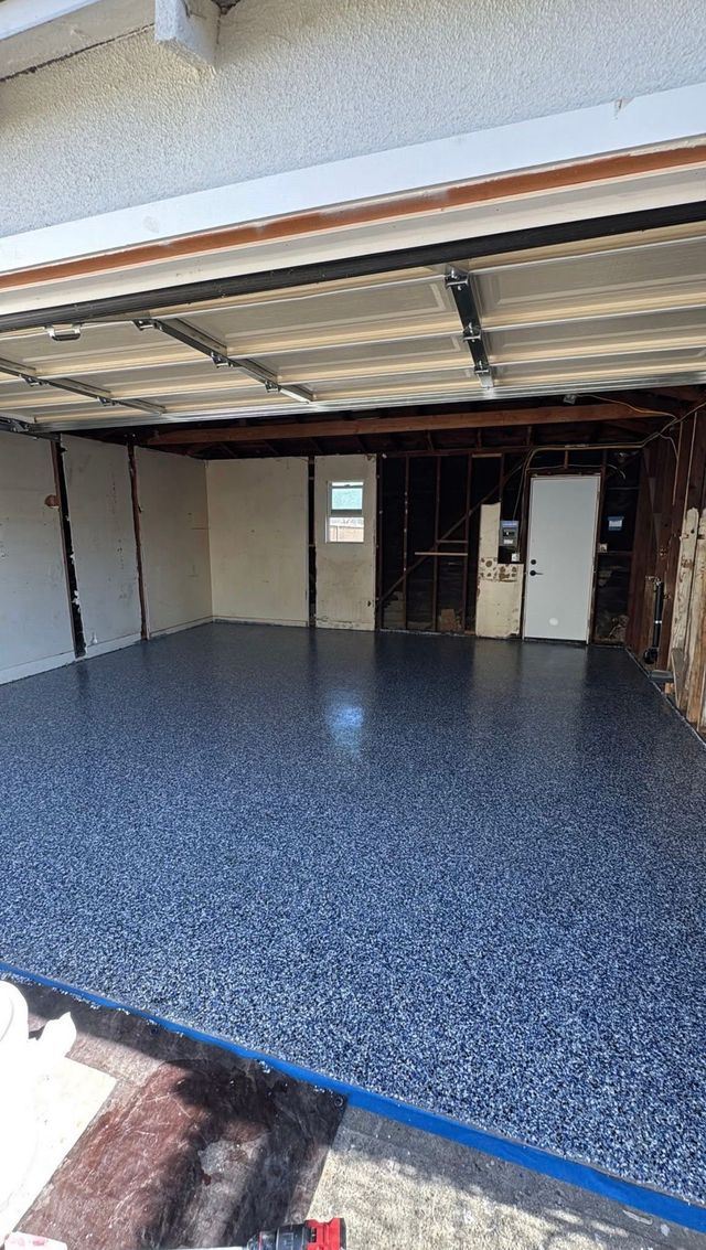 Worker applying gray epoxy floor coating in a garage with a roller and paint bucket