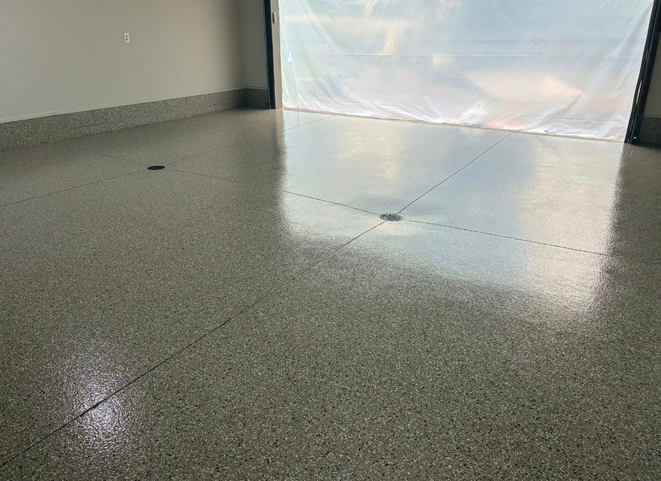 Empty speckled gray floor in a bright room with a white curtain and reflected light near the wall