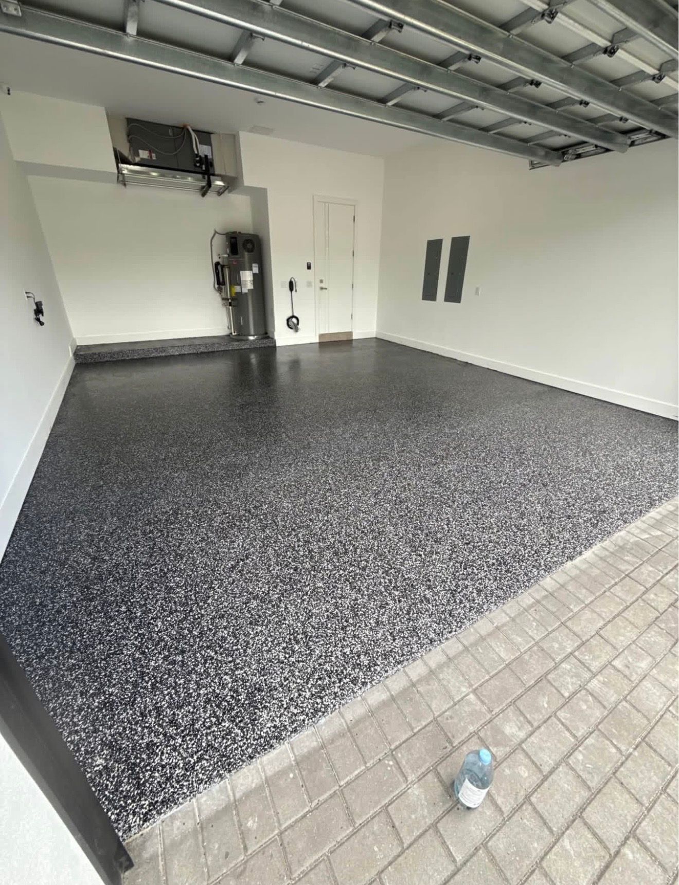 Empty garage with speckled floor coating, white walls, and a small water bottle near the foreground.