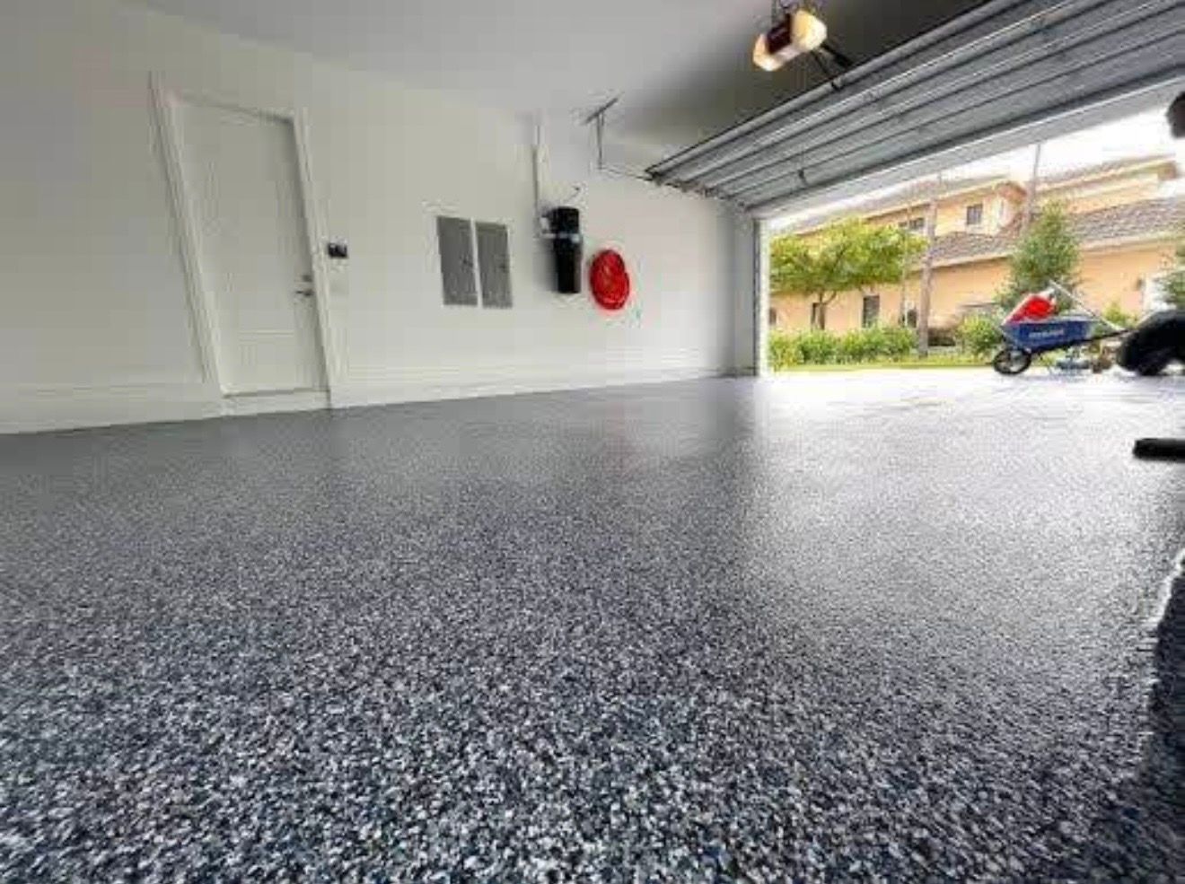 Empty speckled epoxy garage floor with open door to driveway and house exterior.