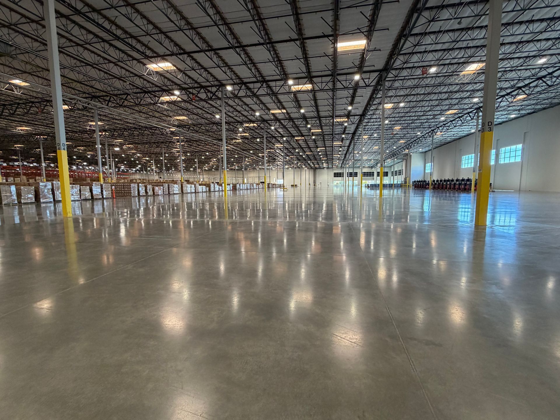 Empty warehouse interior with glossy concrete floor, exposed ceiling grid, and rows of support columns.