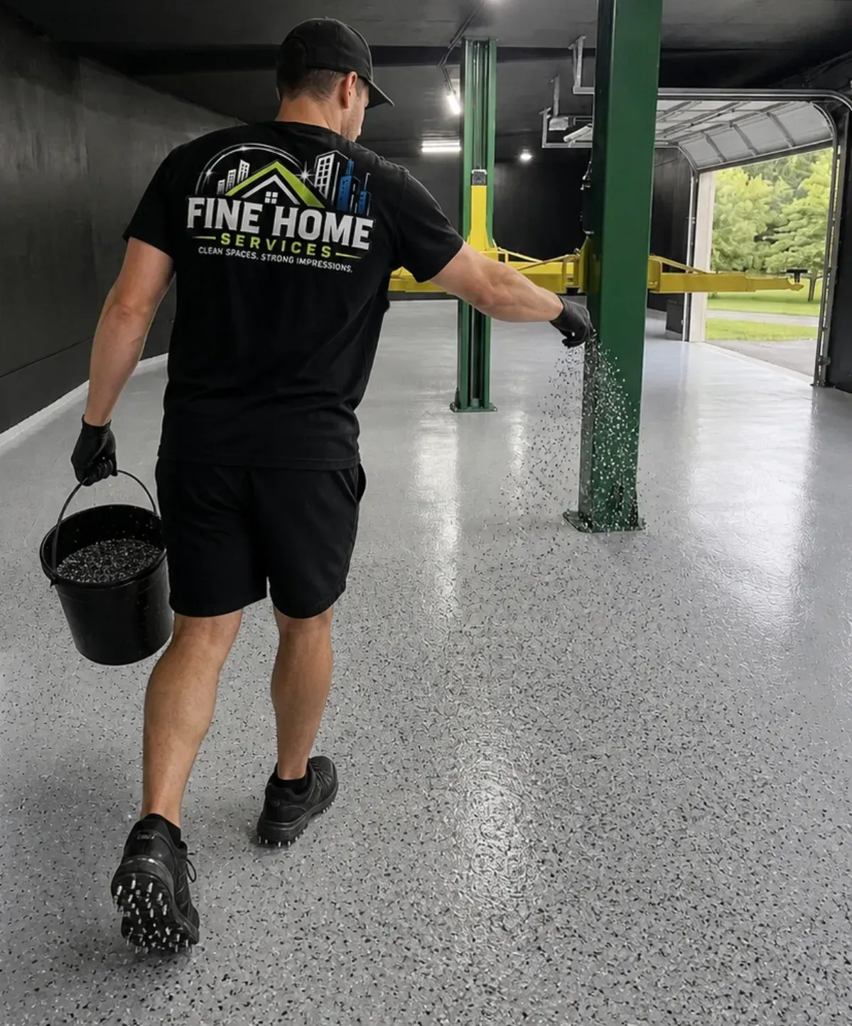 Worker in black uniform cleaning a covered driveway with a bucket and green pressure washer hose