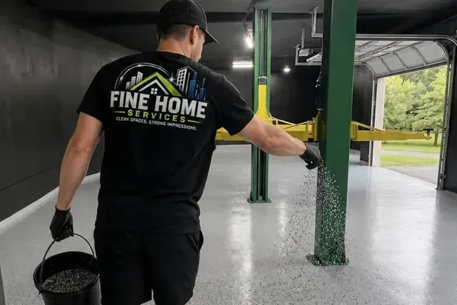 Worker applying gray epoxy floor coating in a garage with a roller and paint bucket