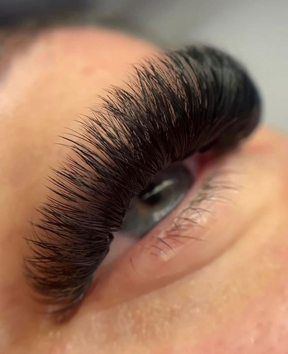 Nahaufnahme eines Auges mit langen, dichten künstlichen Wimpern und einer sichtbaren Augenbraue.