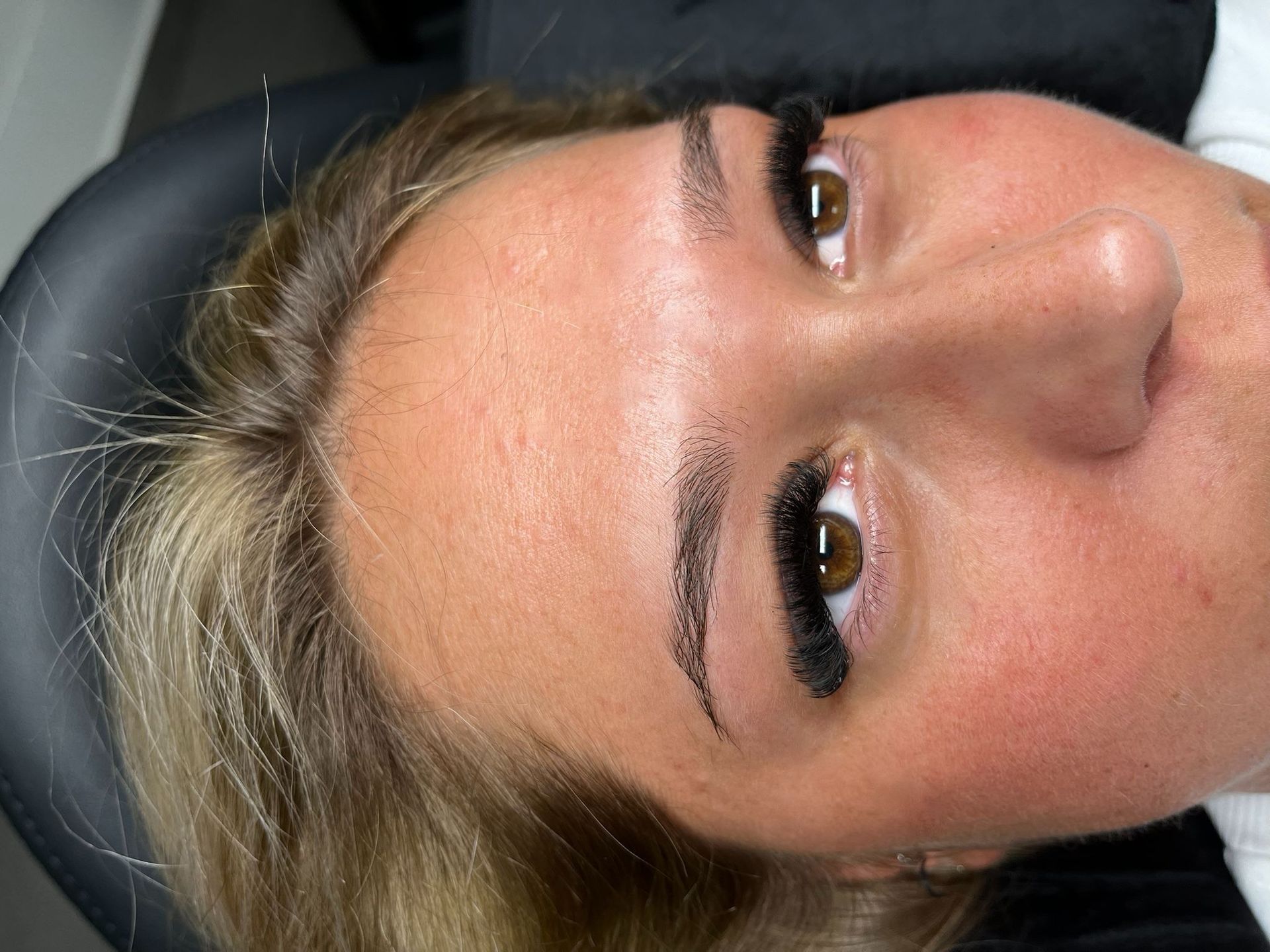 Nahaufnahme eines Personengesichts mit Winged Eyeliner, das vor einem dunklen Hintergrund zur Seite blickt.